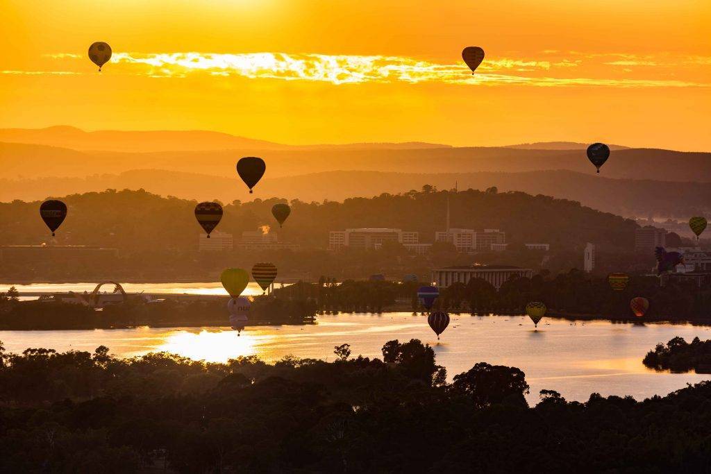 "Colorful hot air balloons filling the sky at dawn during Canberra Balloon Spectacular."